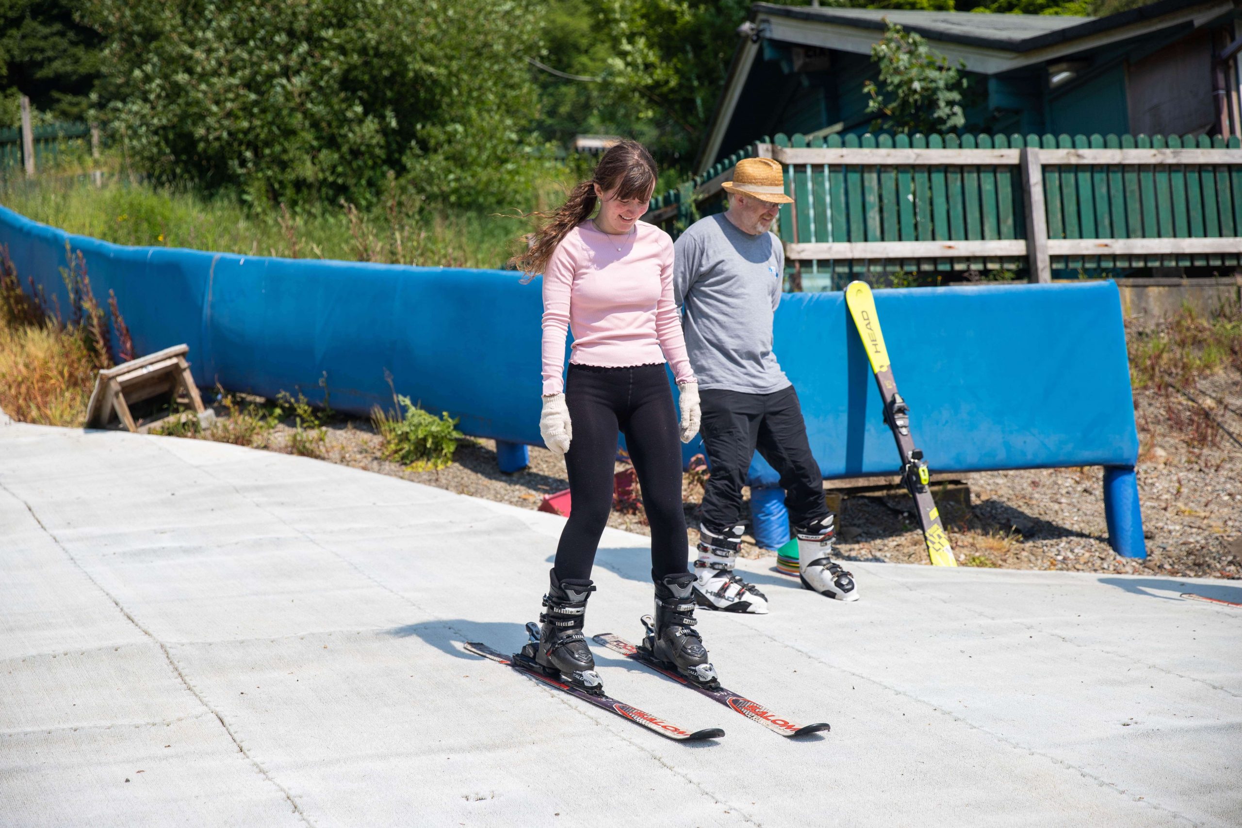 Young girl skiing with Ski instructor Learning the ropes: A beginner skier practices on the gentle slopes at Ski Rossendale, guided by an instructor. The bright summer day adds warmth to the experience, making it the perfect time for outdoor learning and fun on the dry ski slope.